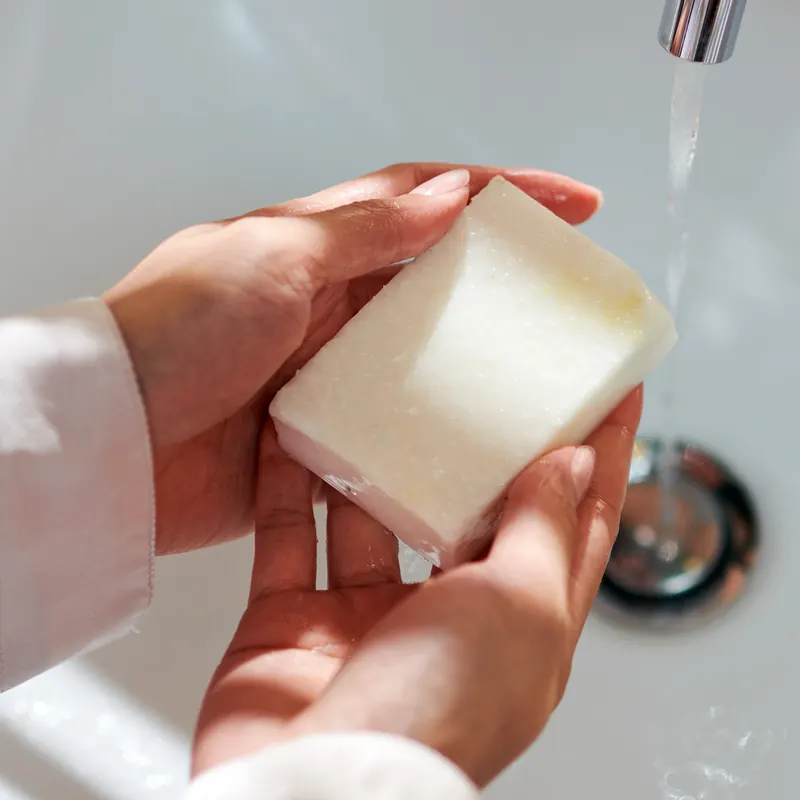 Hands holding a white handmade bar under the tap