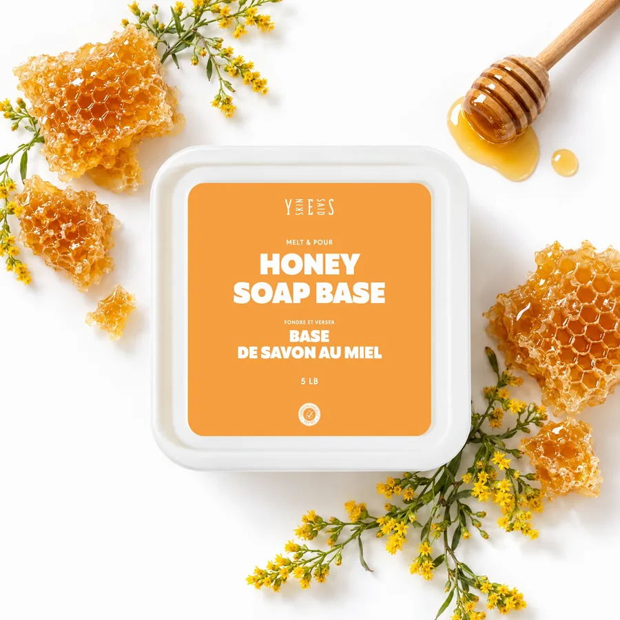 Honey soap base tub from above, with honeycomb, a honey dipper and wildflowers