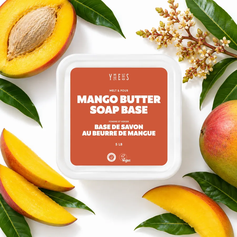 Mango butter soap base tub from above, with mango halves, slices, leaves and blossom