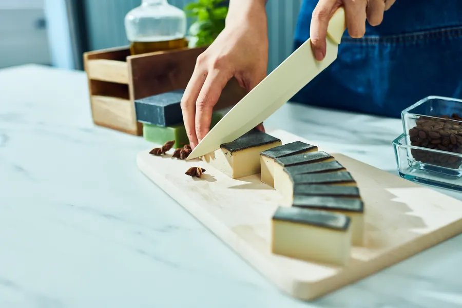 A block of soap base being cut into cubes on a board