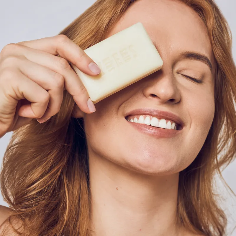 Smiling woman holding a Skin Said Yes goat milk soap bar over one eye