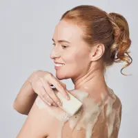 Woman lathering a goat milk soap bar on her shoulder
