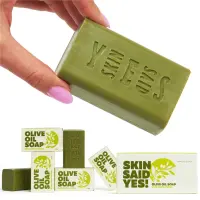 Hand holding a green olive oil soap bar above its boxes