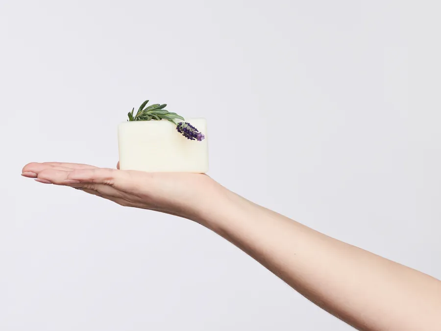 Hand holding a soap bar topped with a lavender sprig