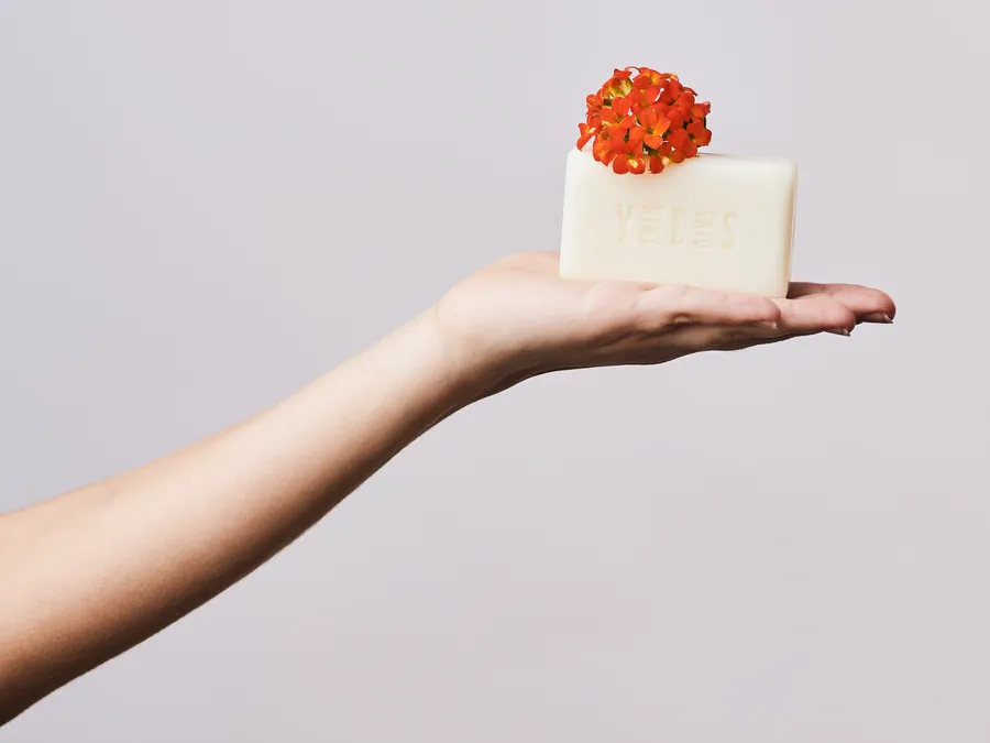 Hand holding a soap bar topped with orange flowers
