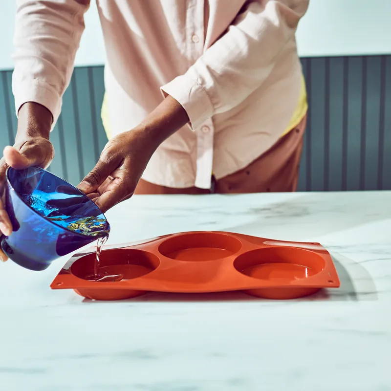 Pouring melted, coloured soap base into a silicone mould